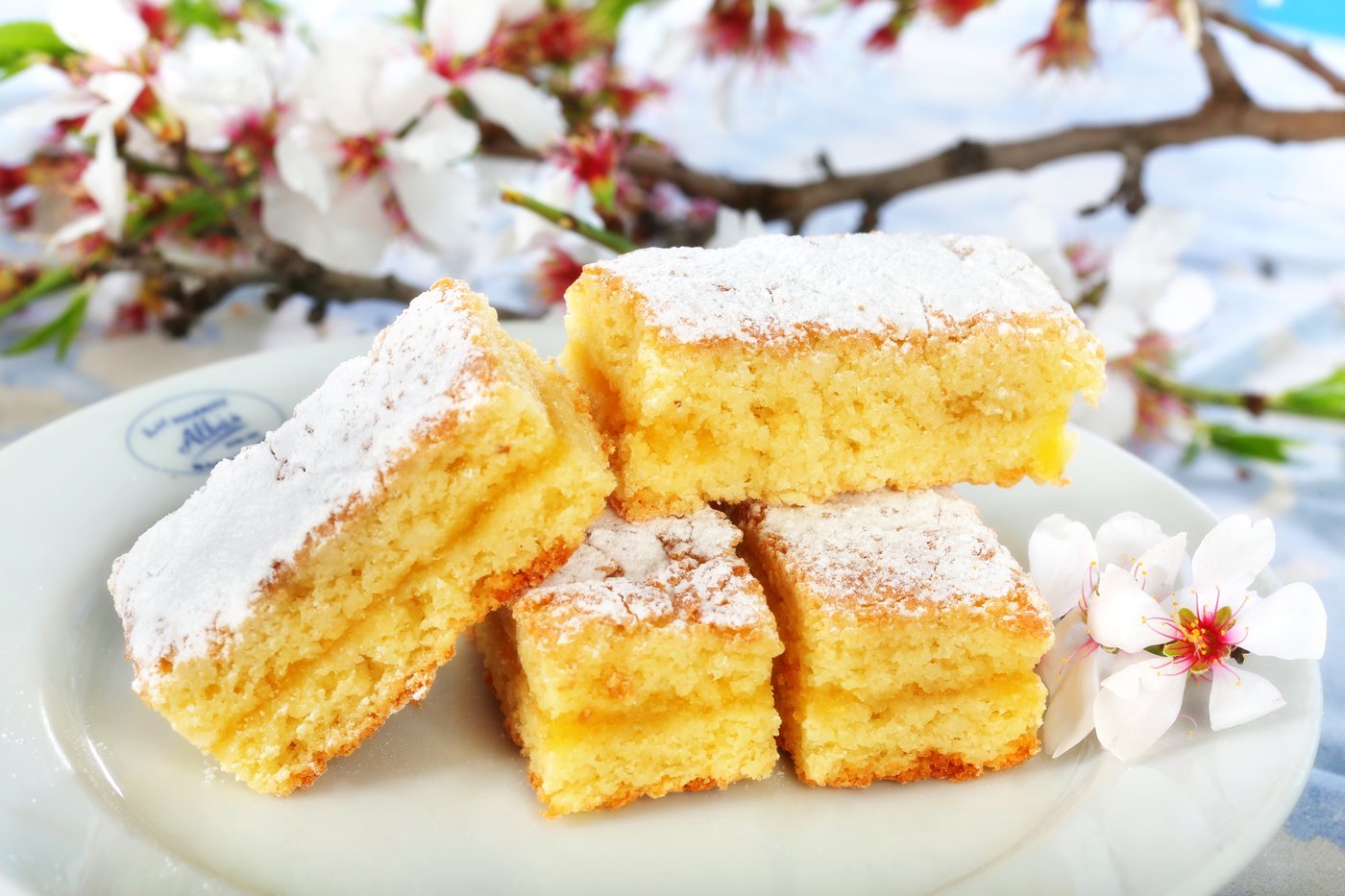 Pasteles Biarritz partidos sobre un plato de Albás, con azúcar glas y flor de almendro