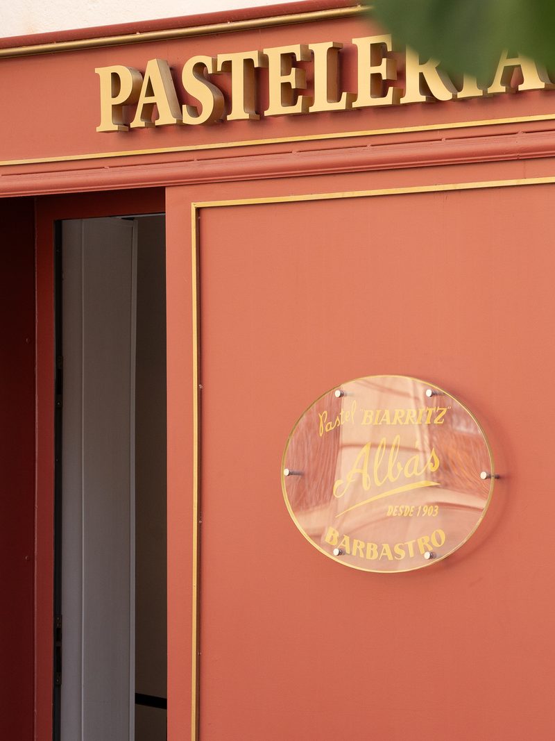 Rótulo dorado de Pastelería Biarritz y placa de Albás en la fachada granate