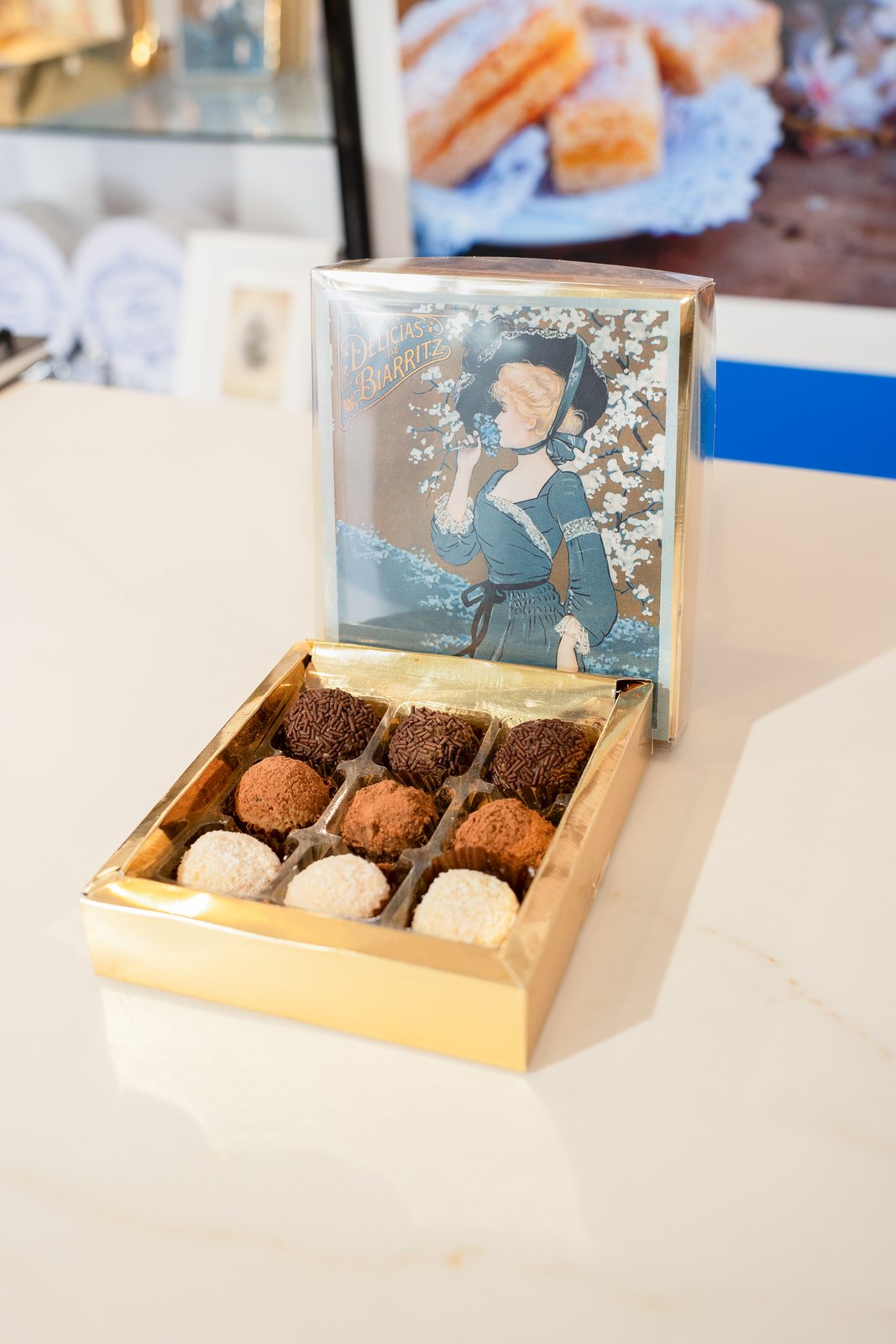 Caja de Delicias Biarritz abierta sobre el mostrador de la pastelería, con la lámina modernista en la tapa