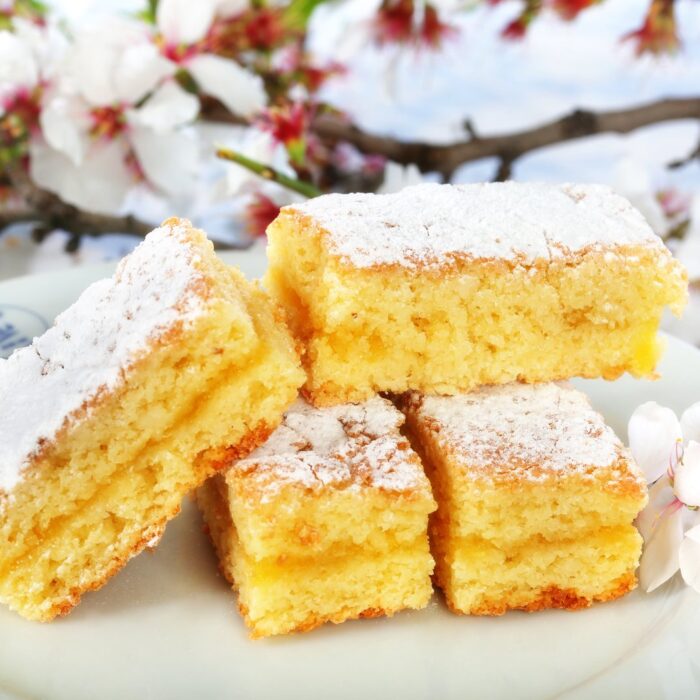 Pasteles Biarritz partidos sobre un plato de Albás, con azúcar glas y flor de almendro
